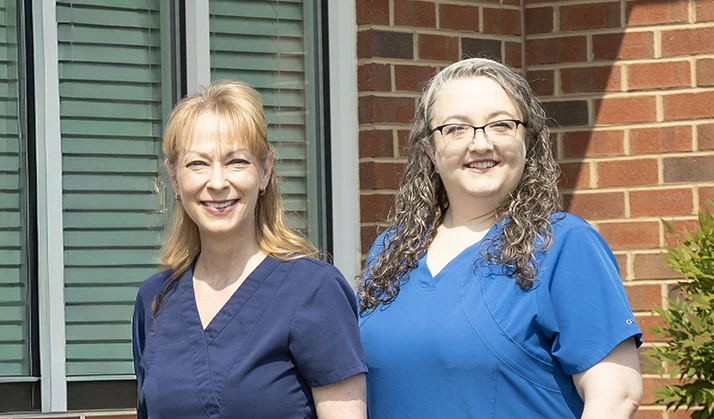 Chiropractor Richmond VA Carmen Johanning Cara Zellner Team Page Carmen Johanning and Cara Zellner smiling outside in front of a brick wall.